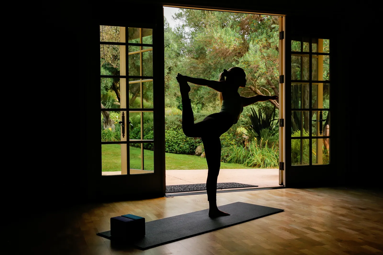 A guest in a dancer's yoga pose, silhouetted against the open garden doors