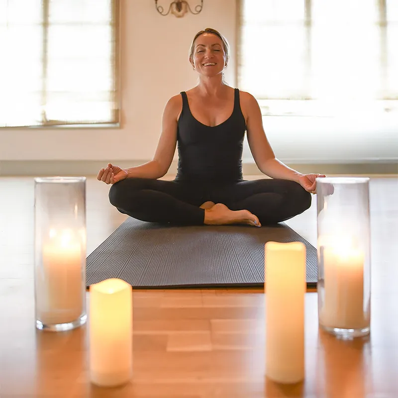 a woman sitting on a yoga mat with candles around her