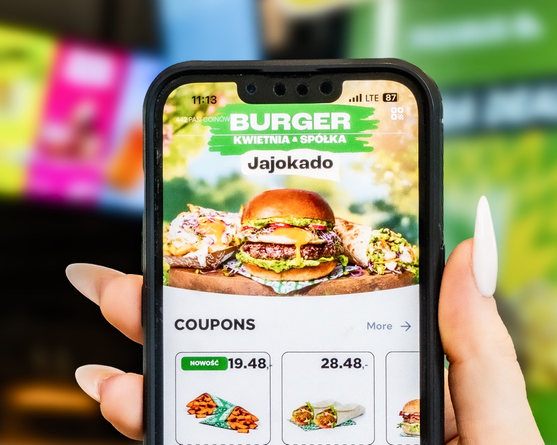 Guest holding a phone showing restaurant coupons in front of a kiosk