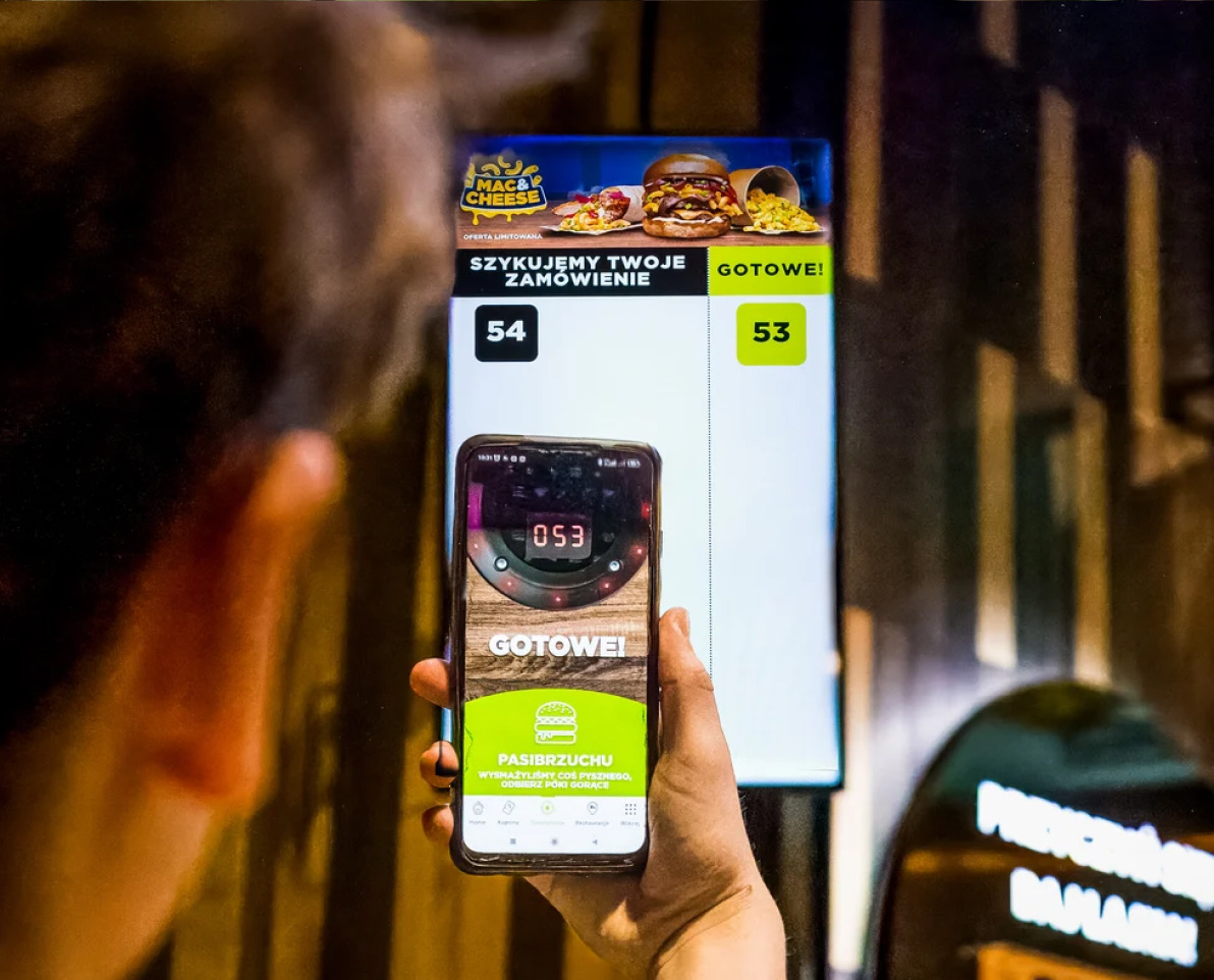 Guest checking an order status on a phone in front of an order ready screen
