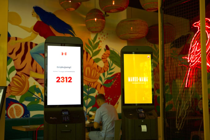 Two Mango Mama self-service kiosks, one showing an order number