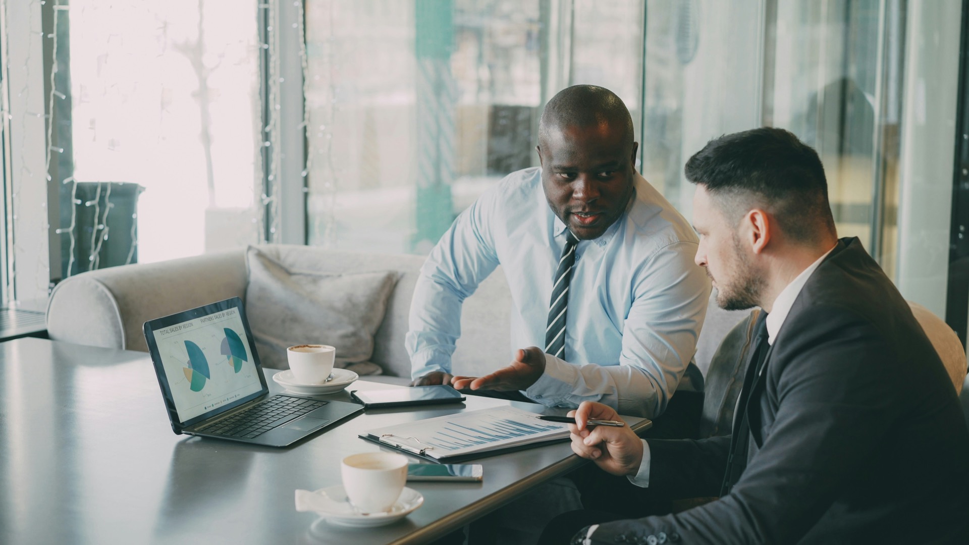 Two consultants reviewing sales charts on a laptop in a meeting.