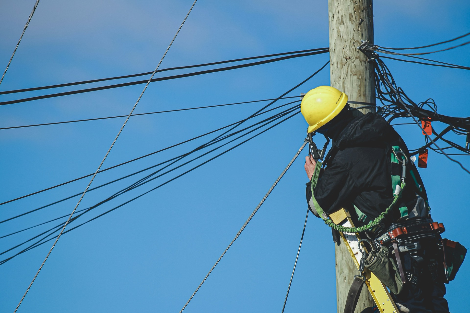 A telecommunications lineman working on overhead cables atop a utility pole.
