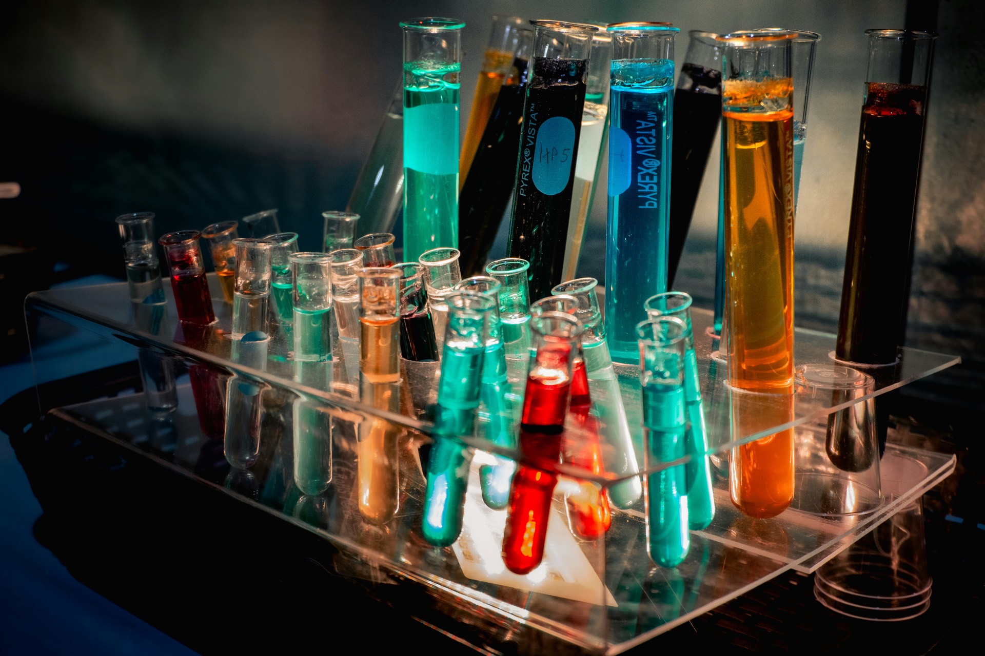 A rack of test tubes filled with brightly coloured chemical solutions in a lab.