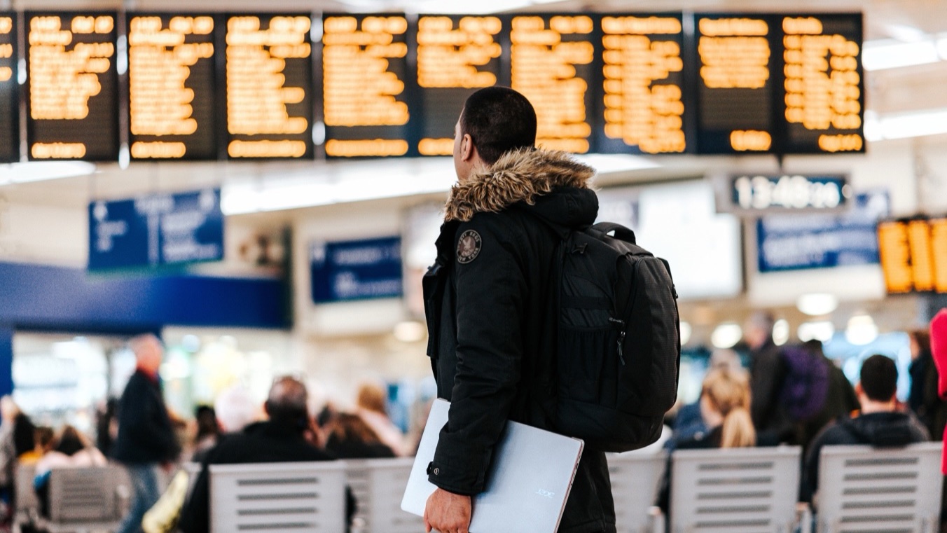 An employee with a laptop and backpack looking at a departure board