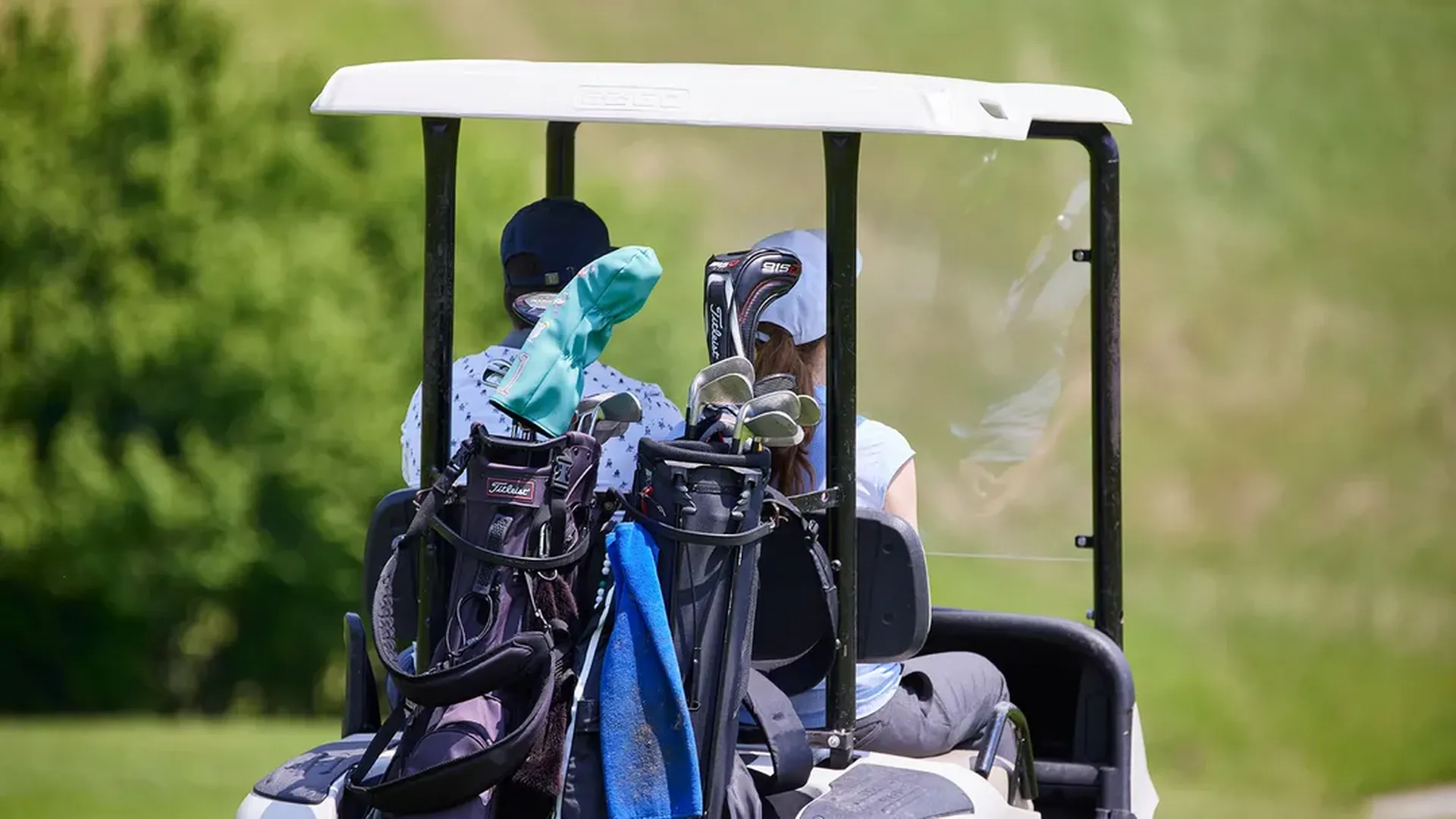 Zwei Personen fahren mit Golfcart und Golftaschen über den Platz