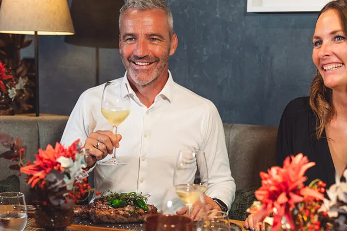 Lächelndes Paar beim Abendessen im Restaurant mit Wein und Steak. Rote Blumen schmücken den Tisch.