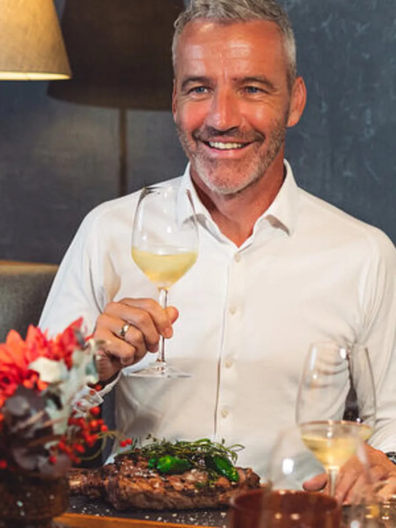 Lächelndes Paar beim Abendessen im Restaurant mit Wein und Steak. Rote Blumen schmücken den Tisch.