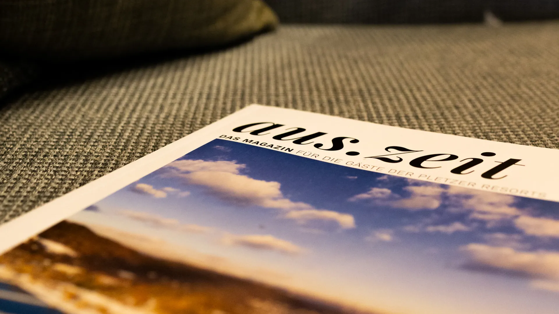 Gästemagazin 'aus.zeit' liegt auf einer Couch mit Kissen