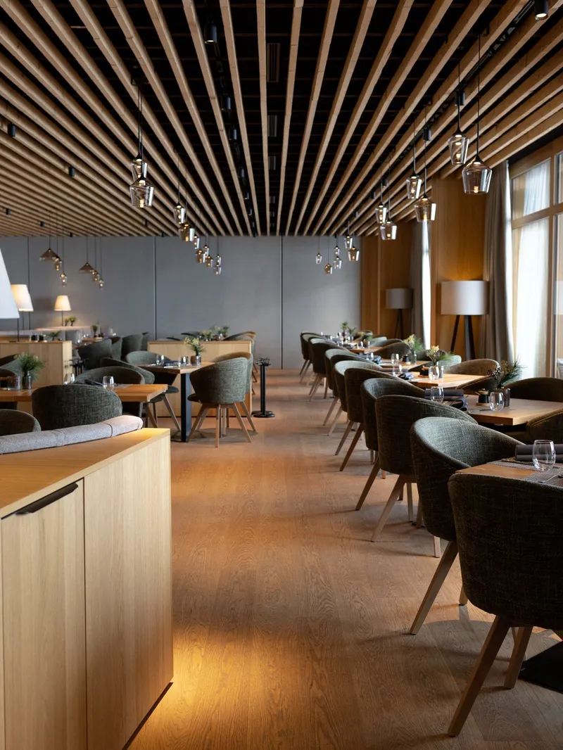 Restaurant mit Holzlamellen-Decke, gepolsterten Stühlen und gedeckten Tischen
