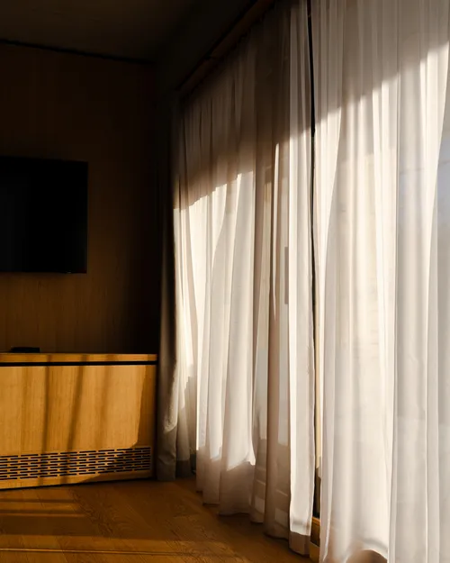 Sonnenlicht fällt durch transparente Vorhänge in ein Hotelzimmer mit Holzboden