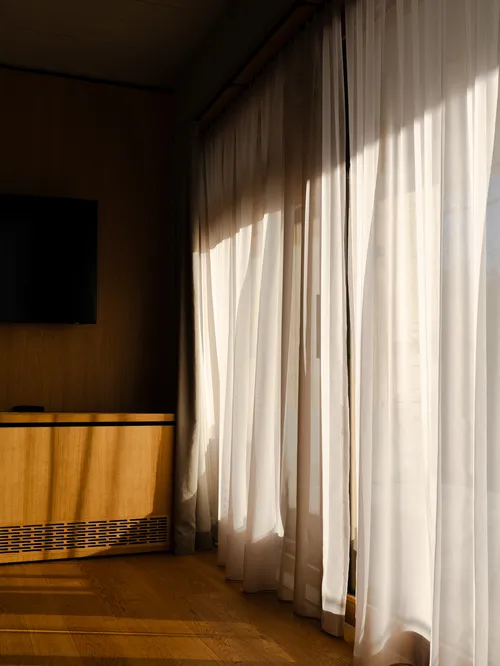 Sonnenlicht fällt durch transparente Vorhänge in ein Hotelzimmer mit Holzboden