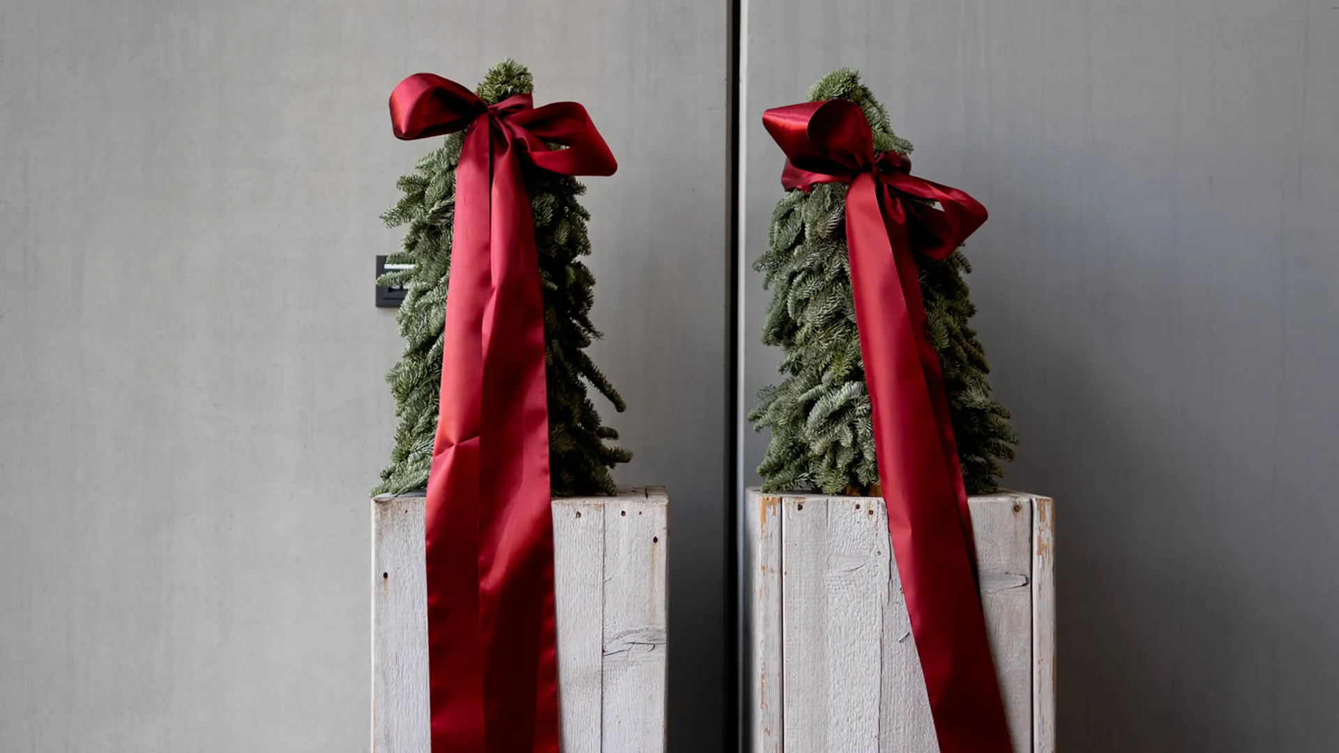 Zwei kleine Weihnachtsbäume mit roten Schleifen auf weißen Holzsäulen