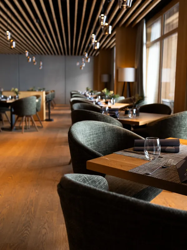 Restaurant mit gedeckten Tischen, gepolsterten Sesseln und Holzlamellendecke