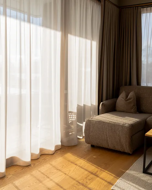Zimmer mit Sofa, transparenten Vorhängen und Sonnenlicht auf Holzboden