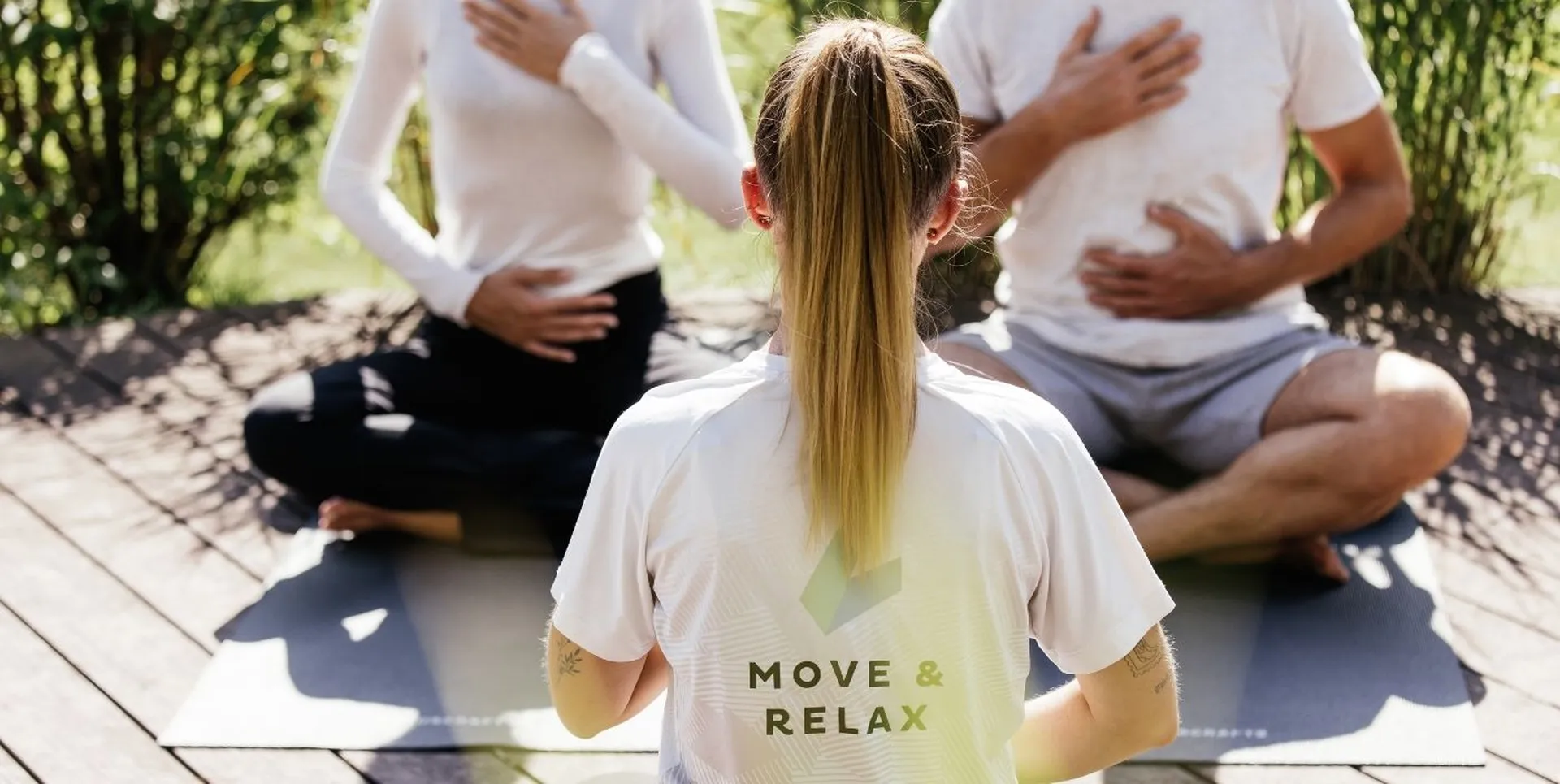 Yogalehrerin leitet Atemübung mit zwei Teilnehmern im Freien