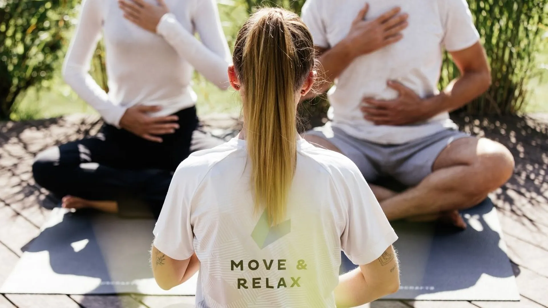 Yogalehrerin leitet Atemübung mit zwei Teilnehmern im Freien