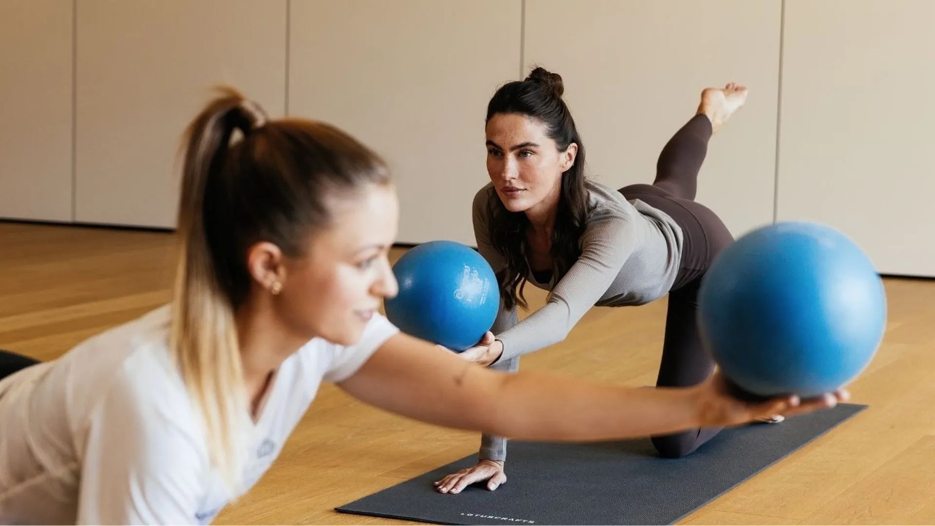 Zwei Frauen trainieren mit blauen Bällen im Vierfüßlerstand auf einer Yogamatte