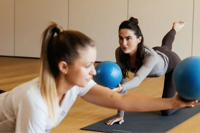 Zwei Frauen trainieren mit blauen Bällen im Vierfüßlerstand auf einer Yogamatte