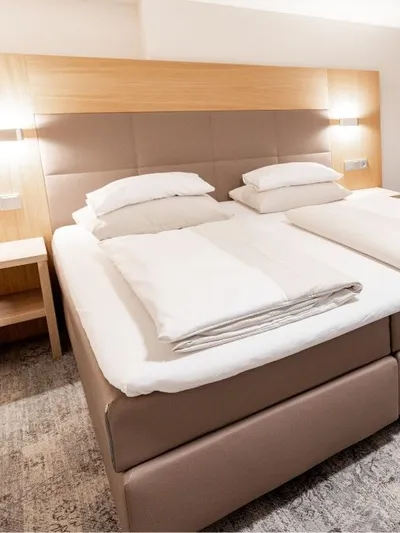 Hotelzimmer mit Doppelbett, Polsterkopfteil und grauem Teppichboden