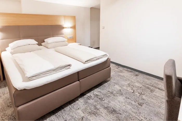 Hotelzimmer mit Doppelbett, Polsterkopfteil und grauem Teppichboden