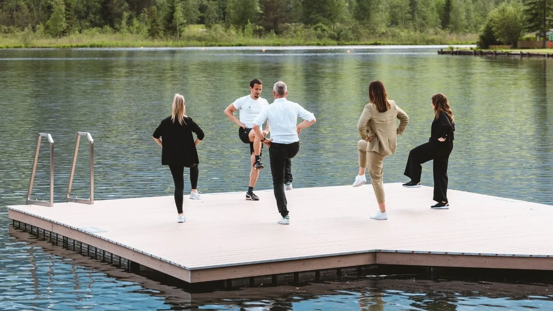 Gruppe macht Dehnübungen auf einem Steg am See