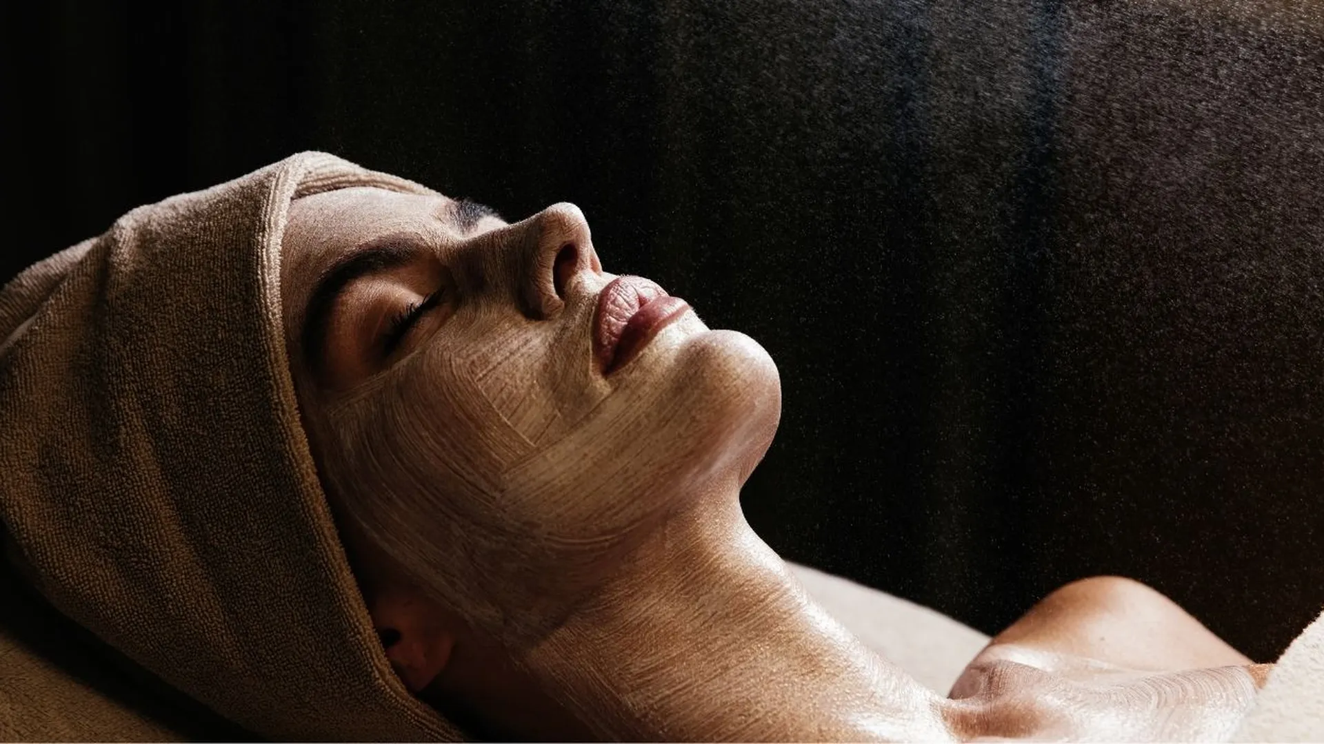 Frau mit Gesichtsmaske und Handtuch entspannt bei einer Spa-Behandlung