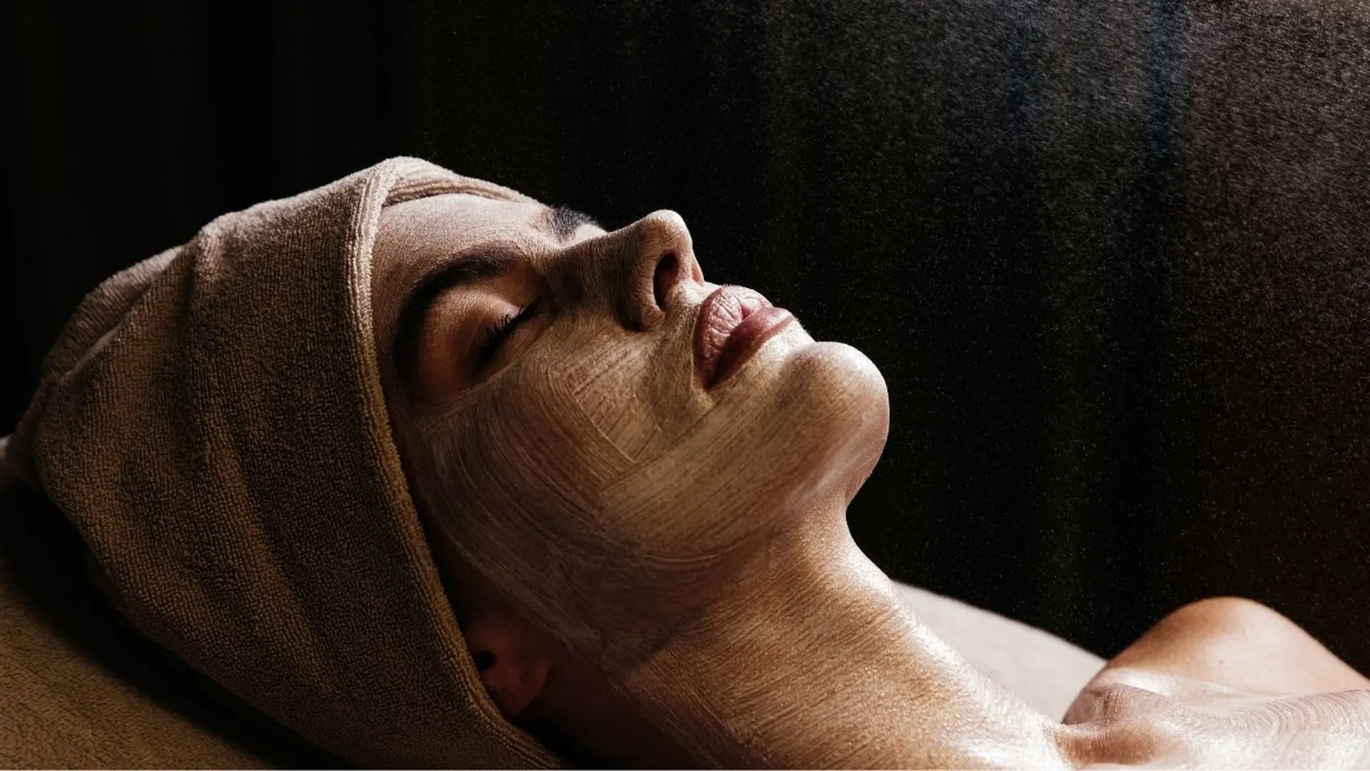 Frau mit Gesichtsmaske und Handtuch entspannt bei einer Spa-Behandlung