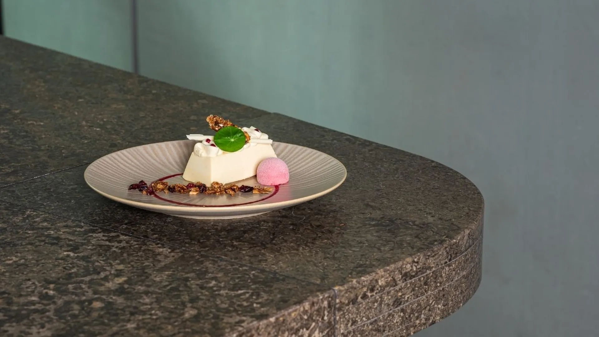 Panna Cotta mit Fruchtsauce, Granola und rosa Sorbetkugel auf Teller