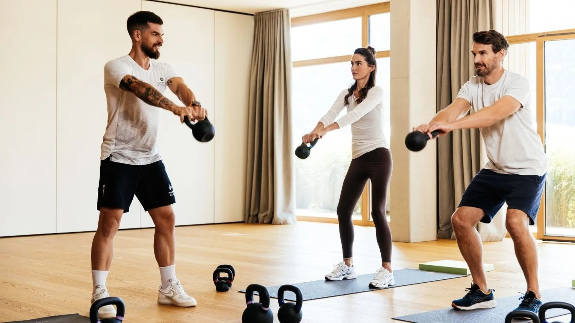 Drei Personen trainieren mit Kettlebells im Fitnessraum