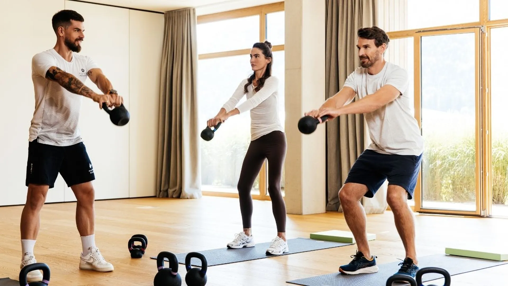 Drei Personen trainieren mit Kettlebells im Fitnessraum