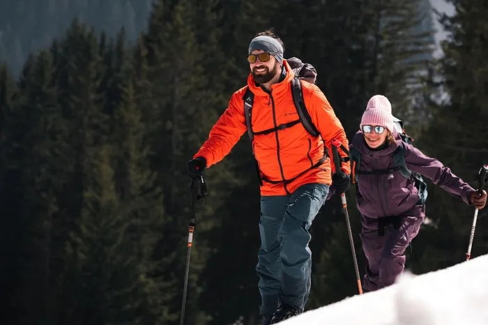 Zwei Personen mit Skiern und Stöcken bei einer Skitour im Schnee vor Nadelwald