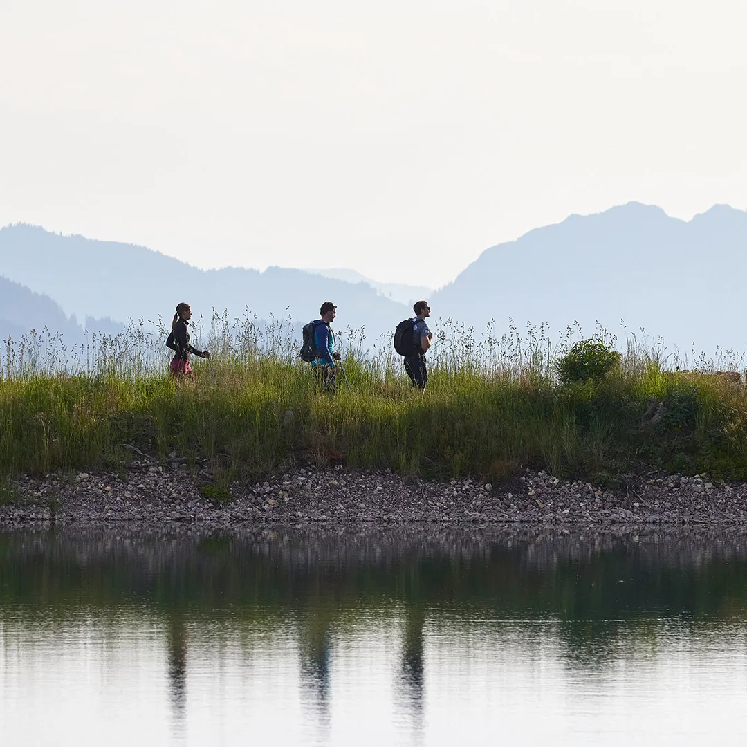 Wanderer am Ufer eines Sees mit Bergpanorama im Hintergrund