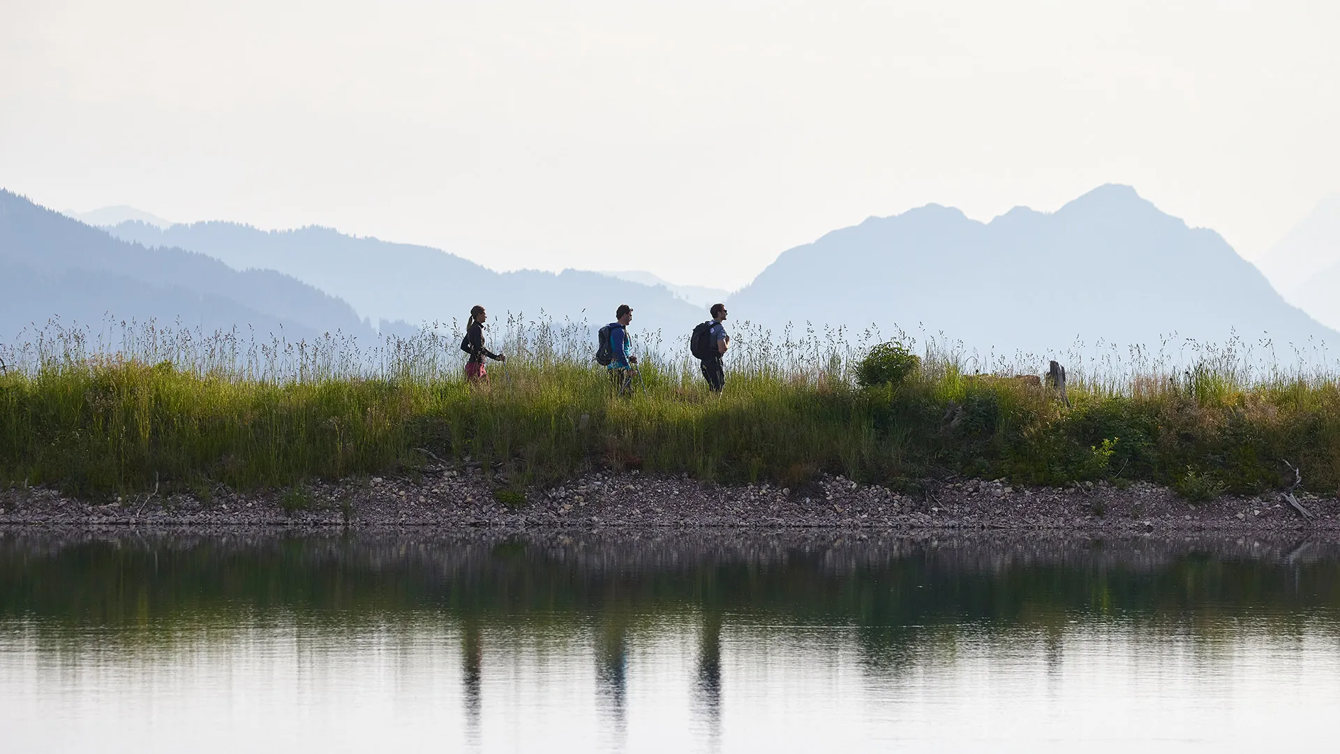Wanderer am Ufer eines Sees mit Bergpanorama im Hintergrund