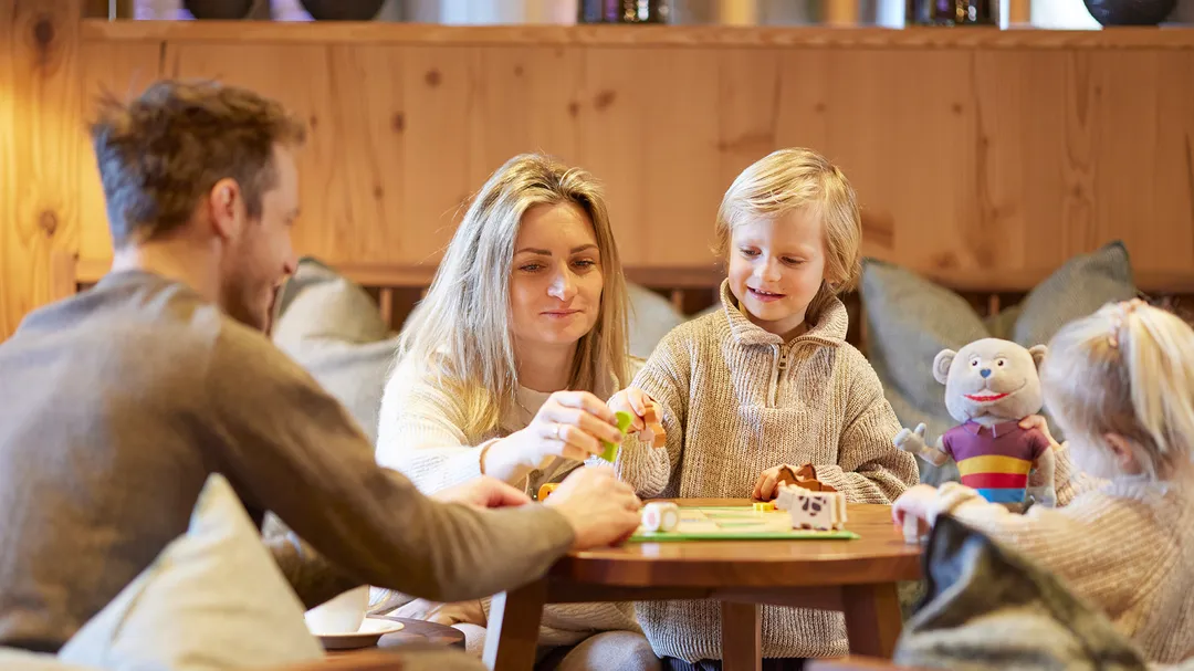 Familie spielt gemeinsam am Tisch in gemütlicher Hotellounge