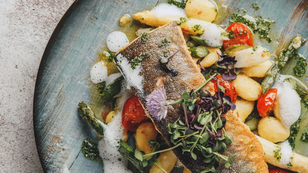 Gebratenes Fischfilet mit Spargel, Kirschtomaten und Kräuterschaum auf Teller