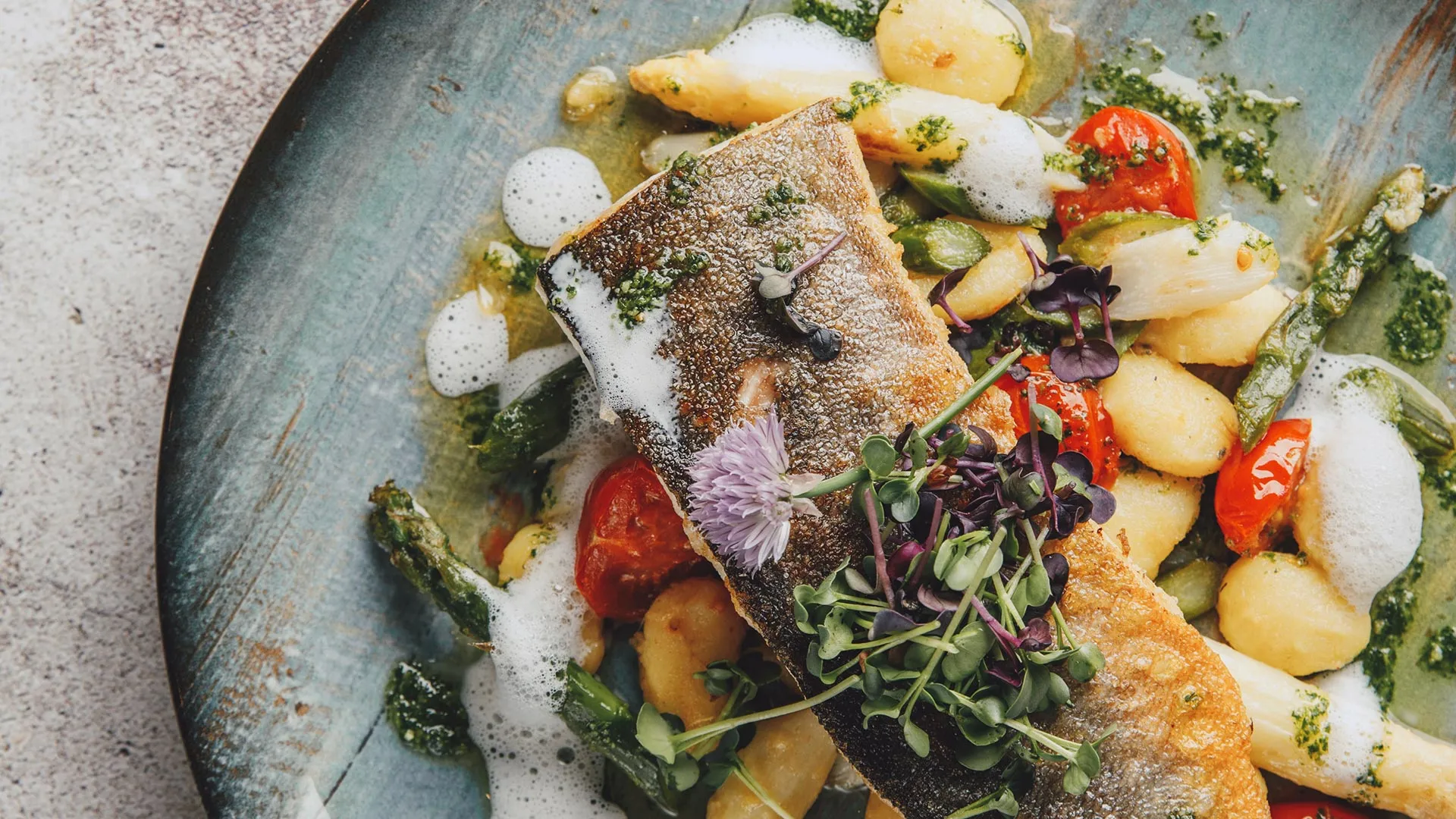 Gebratenes Fischfilet mit Spargel, Kirschtomaten und Kräuterschaum auf Teller