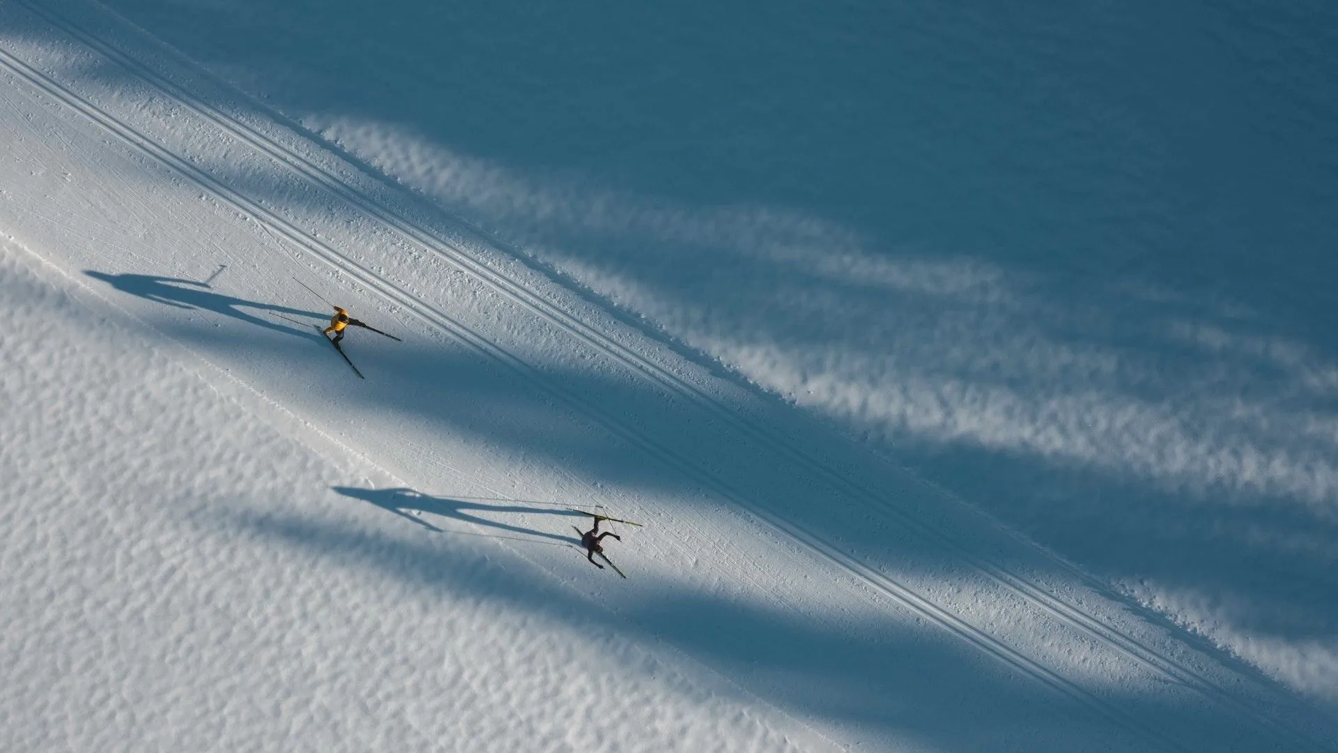 Luftaufnahme von zwei Langläufern auf präparierter Loipe im Schnee