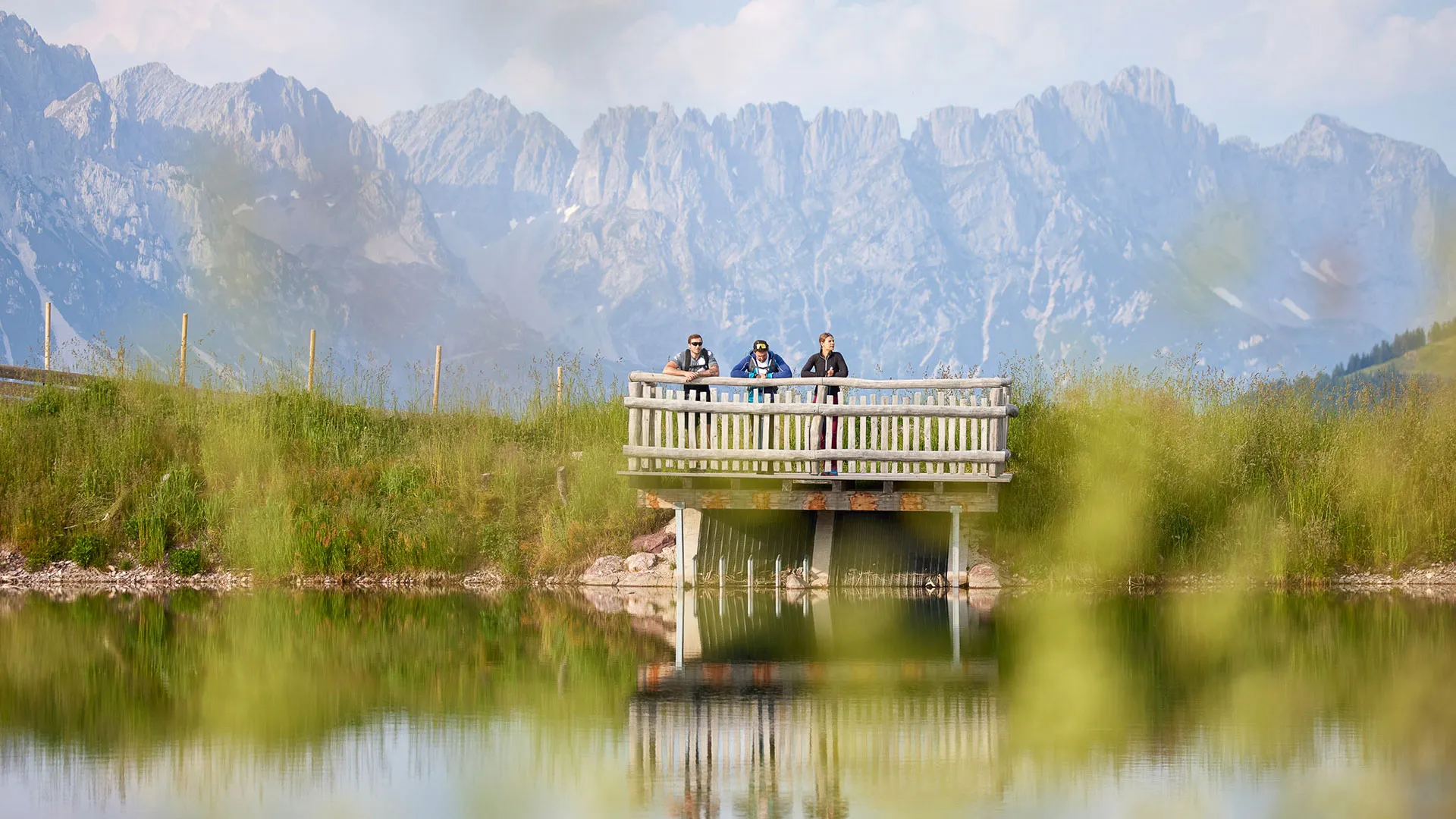 Wanderer auf Aussichtsplattform am See vor Bergpanorama