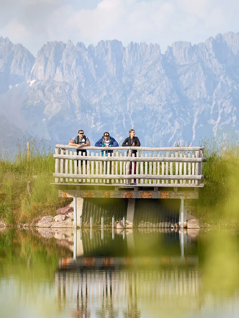 Wanderer auf Aussichtsplattform am See vor Bergpanorama