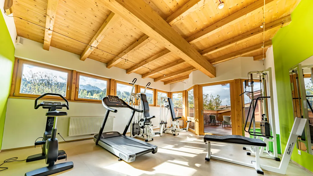Fitnessraum mit Holzdachkonstruktion, Laufband und Trainingsgeräten mit Bergblick