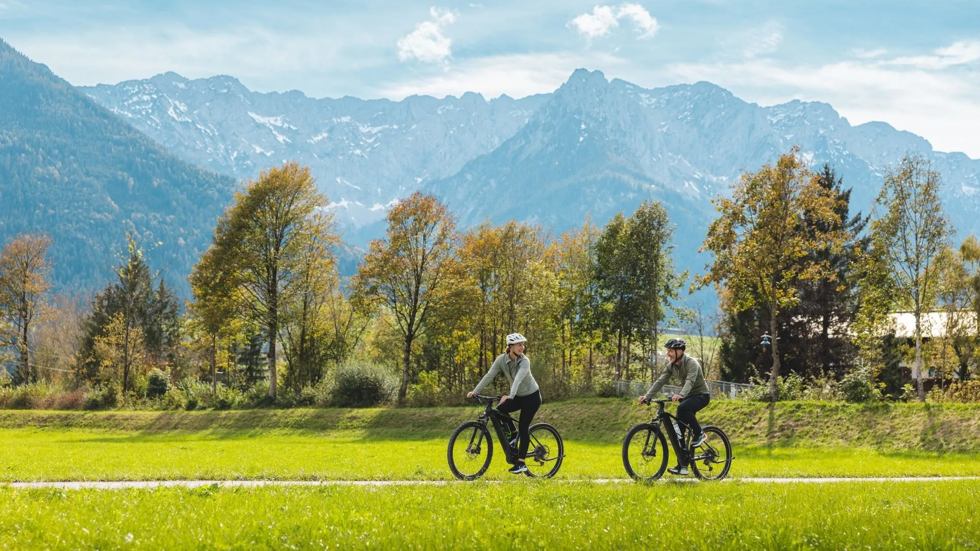 Radfahrer mit Helmen auf Wiesenweg vor Bergpanorama