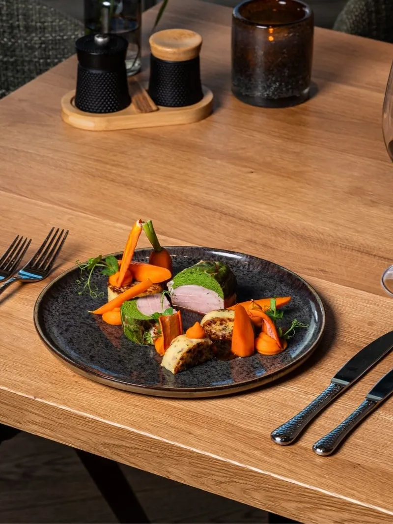 Angerichteter Teller mit Fleisch und Karotten neben Rotweinglas auf Holztisch