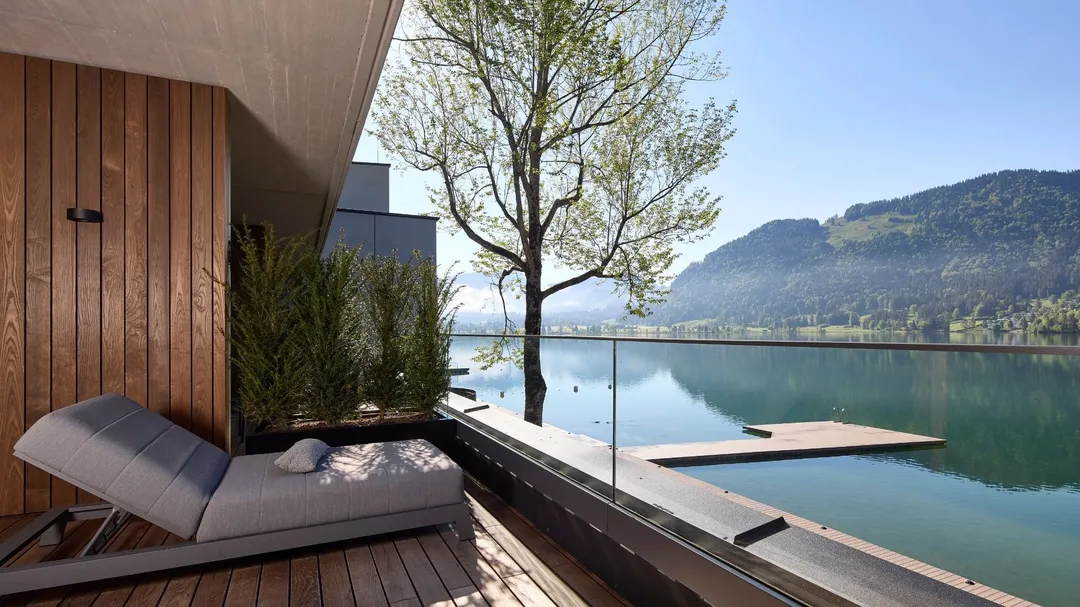 Liegestuhl auf Holzterrasse mit Blick auf See und Berge