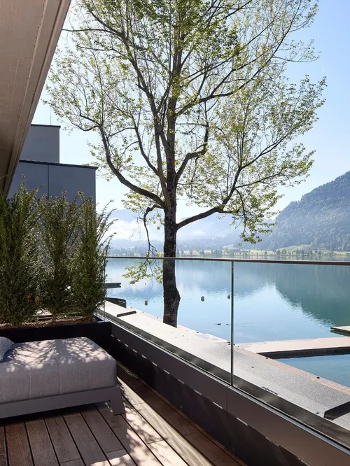 Liegestuhl auf Holzterrasse mit Blick auf See und Berge