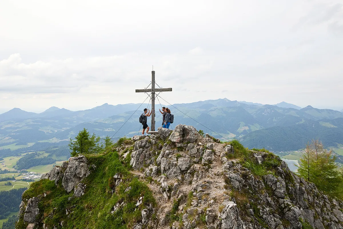 Wanderer am Gipfelkreuz mit Panoramablick über die Berge