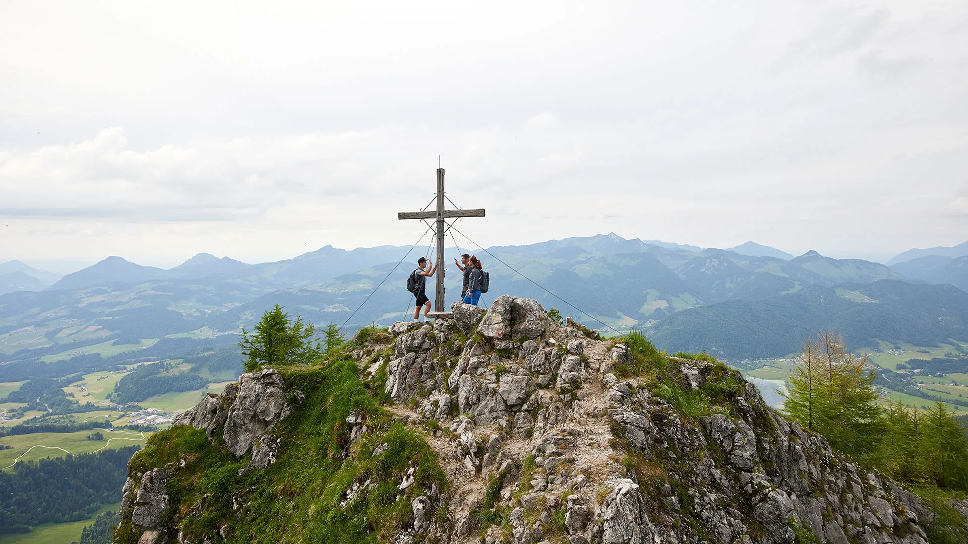 Wanderer am Gipfelkreuz mit Panoramablick über die Berge