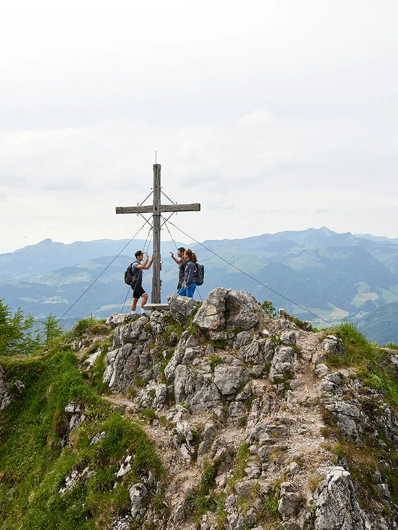 Wanderer am Gipfelkreuz mit Panoramablick über die Berge