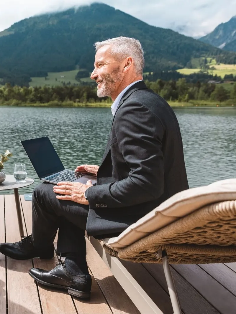 Geschäftsleute mit Laptop auf Terrasse am See vor Bergkulisse