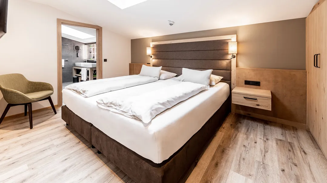 Doppelbett mit Kopfteil aus Holz im Hotelzimmer, Blick ins Badezimmer